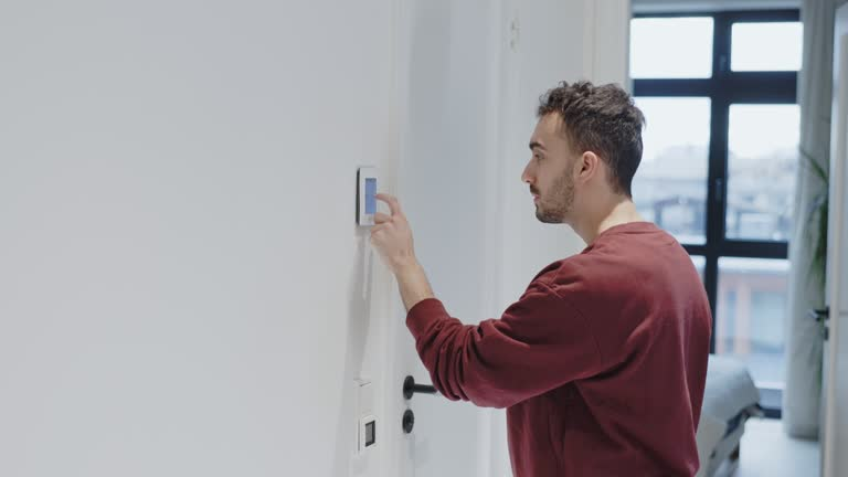 Man adjusting the temperature on a wall-mounted digital thermostat at home