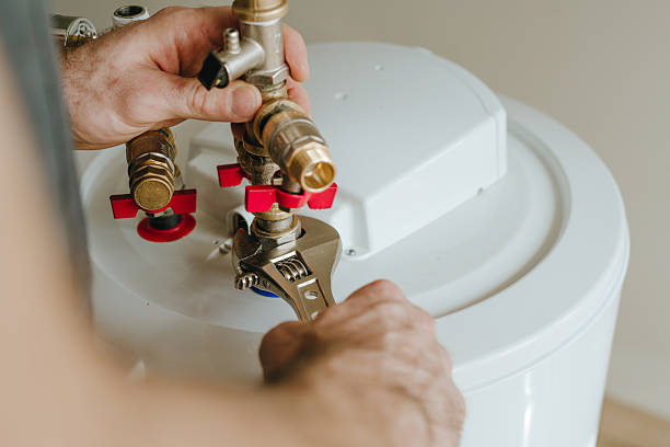 Plumber using an adjustable wrench to tighten brass valve fittings on an electric water heater