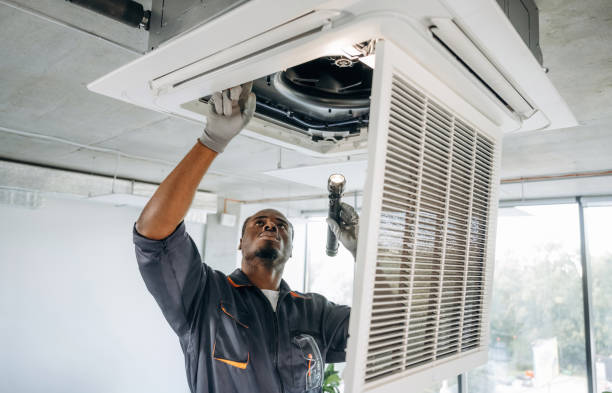 HVAC technician using a flashlight to inspect a ceiling cassette air conditioner with the grille panel open