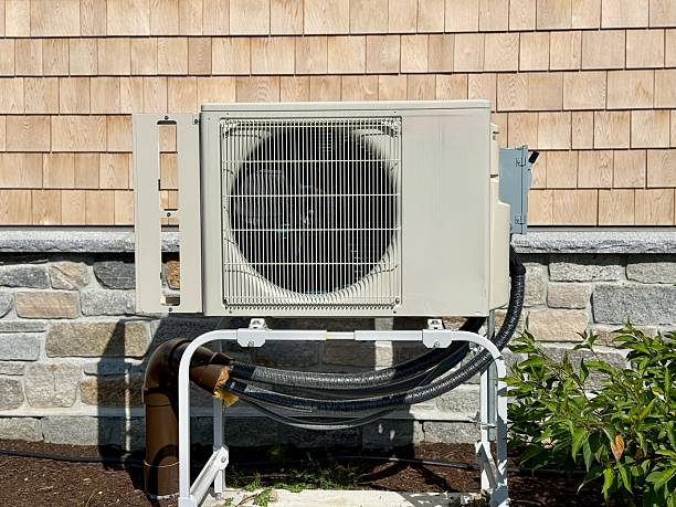 Outdoor mini-split heat pump unit mounted on a metal stand against a shingled and stone exterior wall with insulated line set