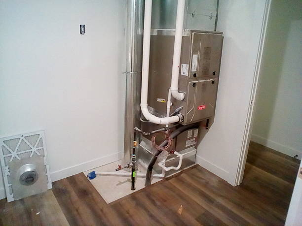 Newly installed furnace with white PVC pipes and copper refrigerant lines in a utility closet with wood-look flooring and an air filter on the floor