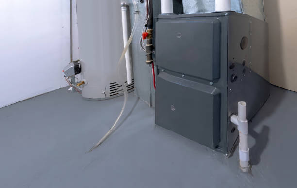 Gray high-efficiency gas furnace with white PVC vent pipes installed in a basement next to a water heater