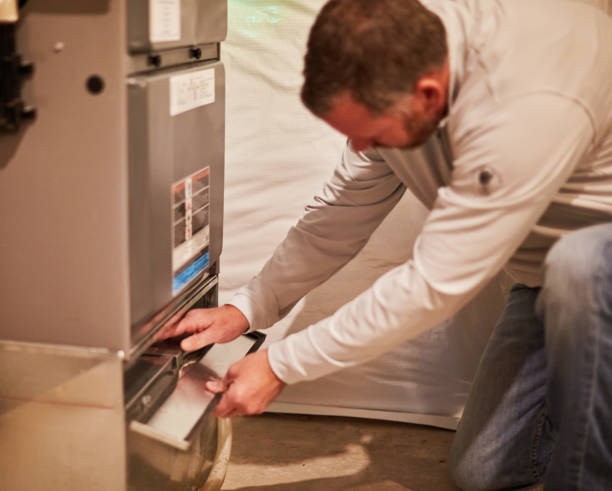 HVAC technician kneeling beside a furnace and opening the lower access panel to service or replace the filter